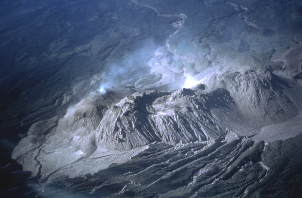 The four major domes of the Santiaguito complex are seen here from the summit of Santa María in 1980. Caliente is degassing to the left, with La Mitad and El Monje in the center, and El Brujo to the right. The dacite dome complex stretches about 3 km in a roughly E-W direction. Lava flows and lahar channels extend down drainages from the dome complex to the south. Photo by Bill Rose, 1980 (Michigan Technological University).