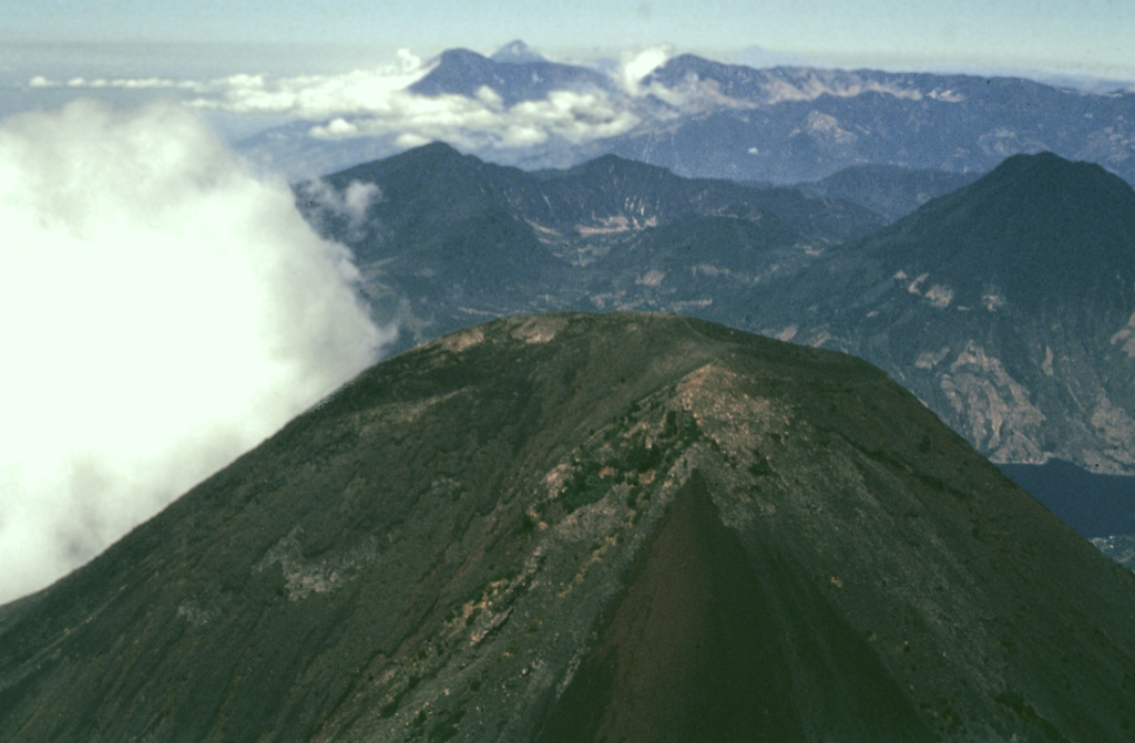 The summit of Atitlán volcano contains shallow craters in this 1980 photo. San Pedro volcano rises across Santiago bay to the right, and in the distance (left-to-right) are the peaks of Santo Tomás, Santa María, and Tajumulco. Atitlán is the highest of the three post-caldera cones of Atitlán caldera. Photo by Bill Rose, 1980 (Michigan Technological University).