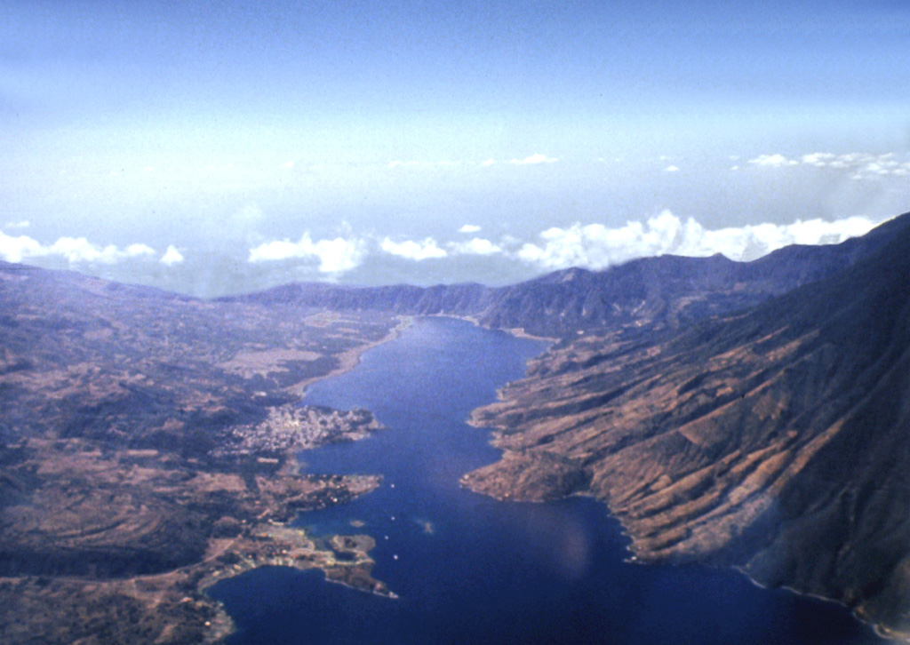 Santiago Bay in Lake Atitlán is the result of encroachment by the flanks of three post-caldera volcanoes into the lake. The narrow channel extends about 8 km to the low southern caldera wall and is about 1 km wide. To the right are the San Pedro flanks, the oldest of the post-caldera stratovolcanoes. Contrasting eruptive styles produced the irregular shoreline in the left foreground consisting of lava flows from Tolimán and the smoother shoreline to the right, formed by pyroclastic deposits from Atitlán. Photo by Bill Rose, 1980 (Michigan Technological University).