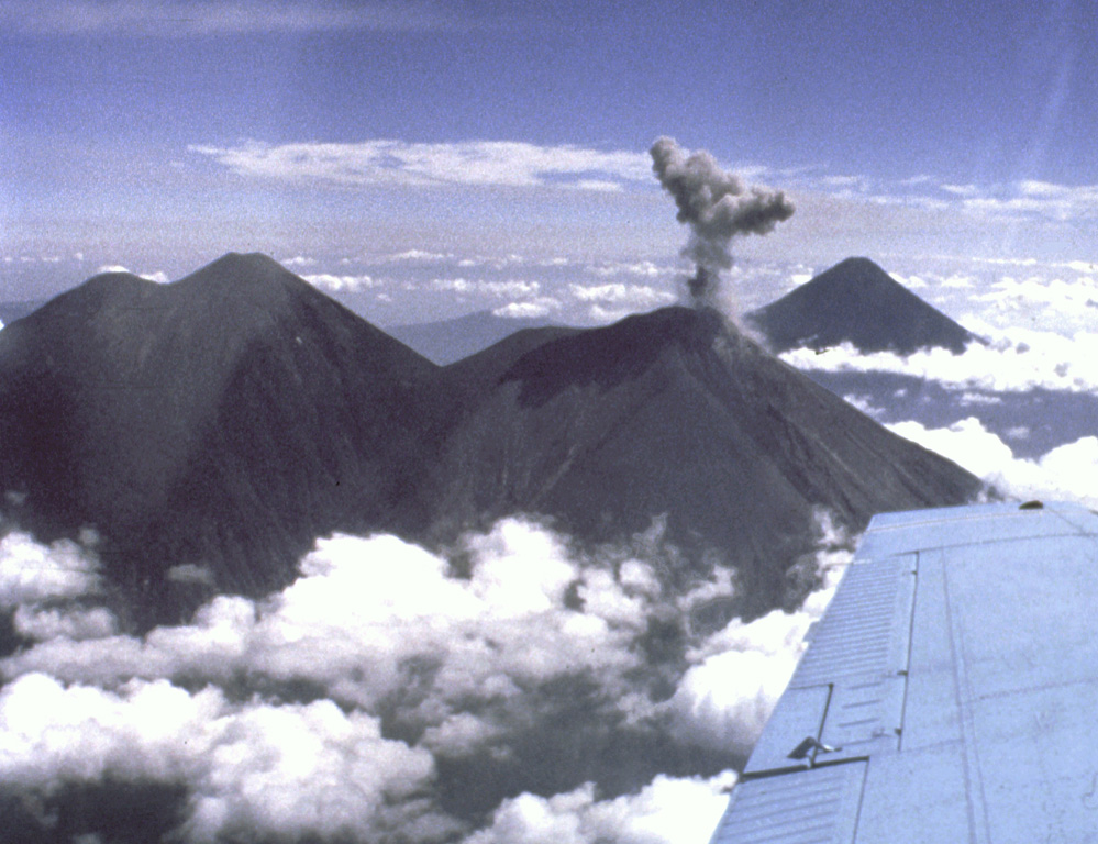 Intermittent explosions took place at Fuego during a two-year-long period beginning in September 1977. Here an ash plume is rising above the summit of Fuego on 11 February 1978. This view is from the WSW, with Acatenango to the left and Agua in the background in 1978. The height of the eruption plume can be compared to the roughly 700 m vertical distance between the summit of Acatenango and the saddle between it and Fuego. Photo by Ray Chuan, 1978 (courtesy of Bill Rose, Michigan Technological University).