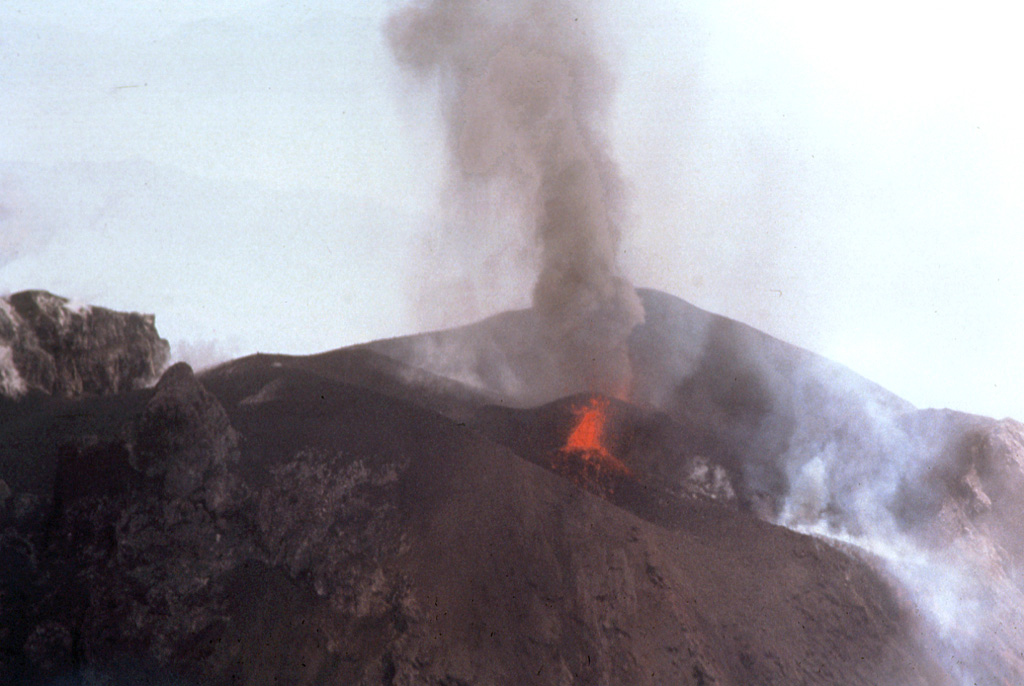 Two vents in the Fuego summit crater were active simultaneously at the time of this 24 February 1978 aerial photograph. A small ash plume rises above the vent at the far side of the crater, while the vent in the foreground ejects lava spatter. This vent feeds a degassing and faintly incandescent lava flow that can be seen to the lower right. Photo by Bill Rose, 1978 (Michigan Technological University).