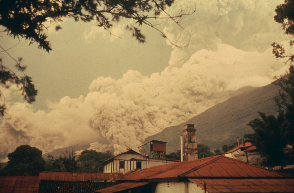 A pyroclastic flow descends drainages on the east flank of Fuego in October 1975 as an ash plume (right) towers above the summit. Intermittent minor eruptions took place 28 May, 23 July to 4 August, and 19 September to 21 October 1975. On 11-12 and 16 October ash fell in, and west of, Antigua. This photo was taken from Finca Capetillo, near Alotenango. Pyroclastic flows frequently travel down these same drainages and had occurred during the two previous eruptions in 1973 and 1974.  Photo by Bill Rose, 1975 (Michigan Technological University).