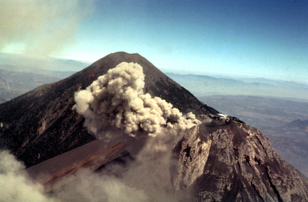 Winds deflect a small 27 February 1978 ash plume from the Fuego summit crater to the west. In the background is Acatenango, which rises about 700 m above the saddle between it and Fuego. Intermittent minor eruptions took place from 11 September 1977 to 8 August 1979, sometimes producing pyroclastic flows and lava flows. Photo by Bill Rose, 1978 (Michigan Technological University).
