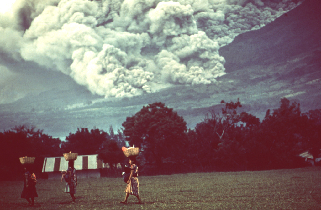 Pyroclastic flows occurred frequently during the October 1974 eruption, and residents of nearby fincas (farms) are seen here carrying goods across a field in front of the pyroclastic flow descending the eastern flank behind them. Despite the frequency and magnitude of the pyroclastic flows, they affected relatively sparsely populated flanks of the volcano and produced no fatalities. Photo by William Buell, 1974.