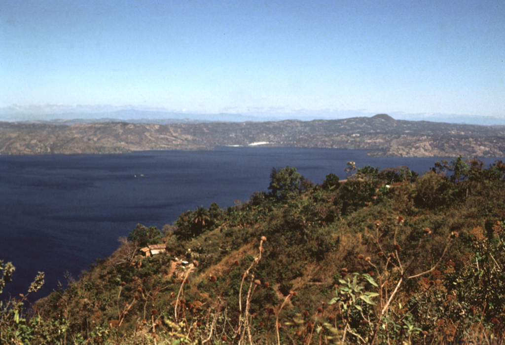 The two tiny islands in the center of Lake Ilopango barely visible above the house in the foreground are the Islas Quemadas. These are post-caldera lava domes that were emplaced from 31 December 1879 to March 1880. A huge ash plume with incandescent ejecta were erupted on 20 January and the dome breached the lake surface on 23 January. It reached a height of 50 m above the lake surface before violent explosions on 5 March destroyed most of the visible part of the dome. Photo by Bill Rose, 1978 (Michigan Technological University).