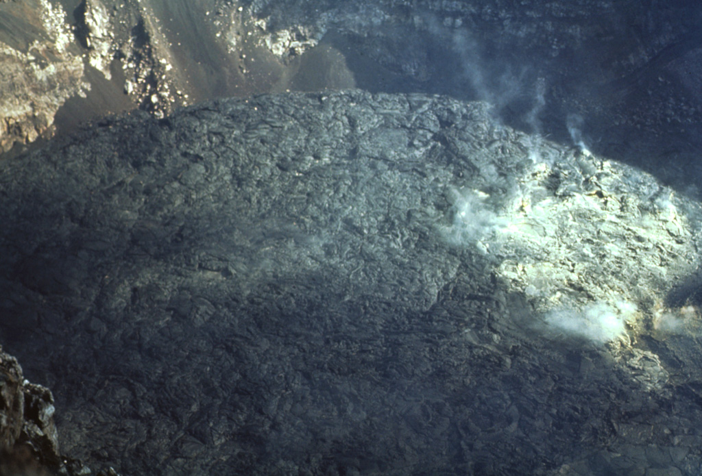 An October 1971 photo from the crater rim shows a fresh black lava flow extruded onto the crater floor.  Fumaroles rise from the surface of the flow at the right.  Masaya began a long-duration eruptive period in 1965.  Several lava flows, such as this one, were erupted between 1965 and 1972.  An active lava lake was visible until 1979, and intermittent small explosive eruptions lasted until 1985. Photo by Bill Rose, 1971 (Michigan Technological University).