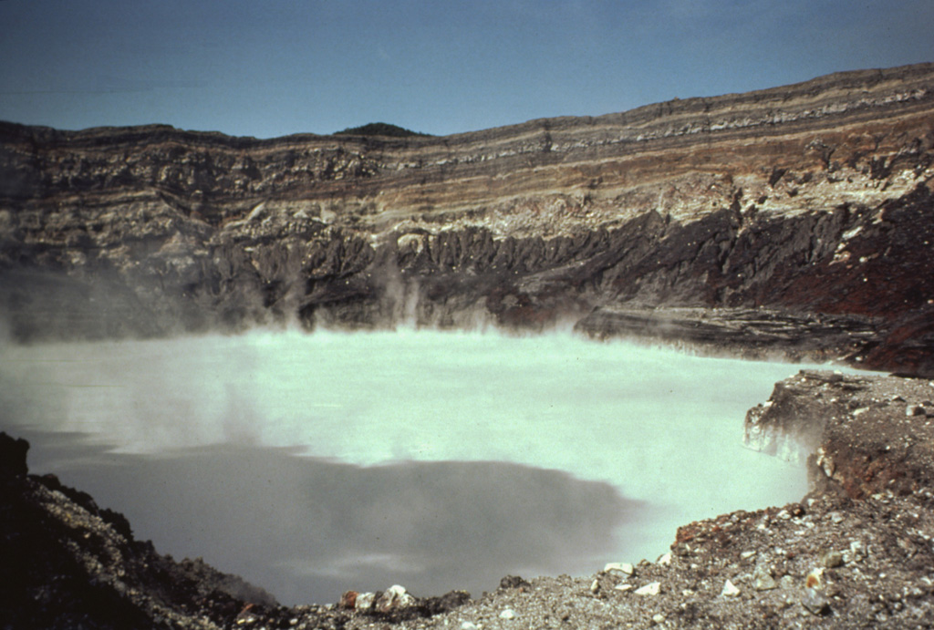 The degassing crater lake at the summit of Poás volcano is seen here in 1982. The 800-m-wide crater lies near the center of the smaller of two calderas at the summit. One of the world’s most acidic natural lakes, the diameter and depth varies with seasonal rainfall and eruptive activity; on occasion the lake has disappeared.  Photo by Bill Rose, 1982 (Michigan Technological University).