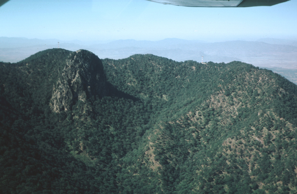 The summit depression of Tequila volcano is breached narrowly to the NE and originated from erosional excavation.  A prominent 300-m-high dacitic spine, left after erosional removal of softer rocks surrounding the vent, forms the dramatic steep-sided peak at the left.  The spine was dated at about 210,000 years and probably represents the latest activity from the central vent.   Photo by Jim Luhr, 1979 (Smithsonian Institution).