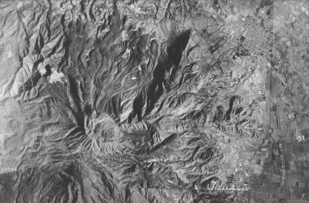 A composite aerial photo with north to the top shows the lighter-gray summit of San Juan volcano just left of the center of the photo.  Cerro Alto, the highest peak of the San Juan complex, forms the dark area at the lower left.  A dark shadow highlights a 5-km-long NE-trending ridge that marks an eruptive fissure of the cone-building stage of San Juan.  Prominent leveed lava flows that reach the northern flank mark the latest eruptive products of San Juan.  The cities of Tepic and Jalisco lie at the upper and lower right, respectively. Photo courtesy of Jim Luhr (Smithsonian Institution).