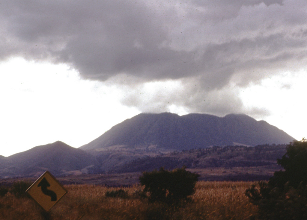 The three coalescing Cerro San Pedro lava domes (center), seen here from the NE, were constructed within the 7 x 10 km wide San Pedro caldera.  The ridge at the left is the eastern rim of the caldera, which cuts andesitic-to-dacitic lava domes of early Pleistocene age.  The dacitic San Pedro lava domes were dated at 0.75-0.80 million years and were constructed along a WNW-trending line.  Two of the domes have partially collapsed, forming large debris-avalanche deposits that reach up to 10 km from the source. Photo by Jim Luhr, 1978 (Smithsonian Institution).