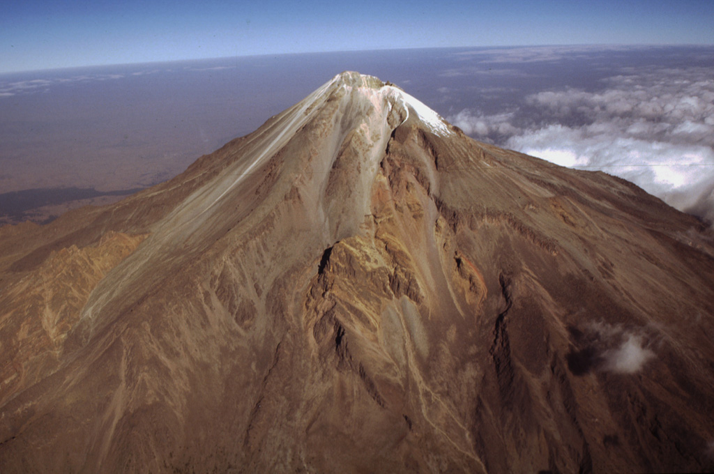 México's highest volcano, Pico de Orizaba, is seen here in an aerial view from the SE. The modern Citlaltépetl cone, marking the upper part of the volcano, was constructed within horseshoe-shaped scarps formed by previous edifice collapse events. The orange-brown ridges at the middle left and center are remnants of the oldest edifice, Torrecillas. The lighter-colored area between these two ridges is a thick, historical, lava flow that was erupted from the modern cone. Photo by Gerardo Carrasco-Núñez, 1997 (Universidad Nacional Autónoma de México).