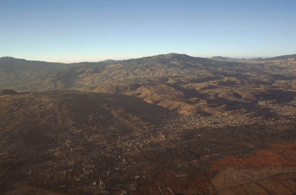 Several volcanoes of the Chichinautzin volcanic field can be seen in this aerial photo from the NE. To the lower left is Volcán Teuhtli with a small cone on its summit to the far left. The lava flow with steep flow boundaries in the center of the photo descending diagonally to the right is the massive Xicomulco lava flow. Volcán Cuauhtzin, in the background to the right, emplaced widespread lava flows.  Photo by Gerardo Carrasco-Núñez, 1997 (Universidad Nacional Autónoma de México).