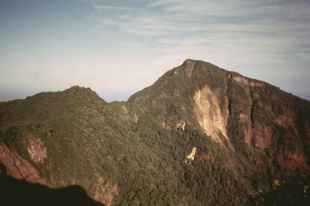 The south side of Mombacho volcano is cut by a large horseshoe-shaped depression that left two major summit peaks.  Recent landslips scar the face of the higher easternmost peak.  The depression was formed during collapse of the volcano, which produced a large debris avalanche that traveled to the south.  The 2-km-wide depression merges with a scarp from a NE-flank collapse, which lies on the other side of the notch in the center of the photo. Photo by Jaime Incer, 1996.