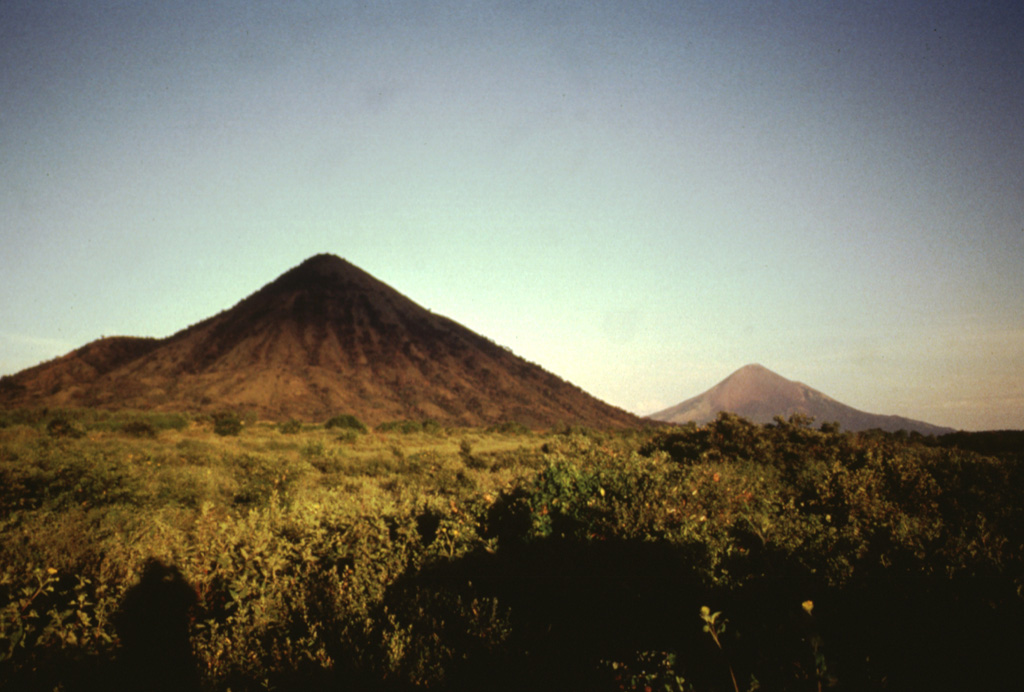 Two conical peaks of differing age rise to the east above the floor of the Nicaraguan depression.  Cerro Asososca (left), part of Las Pilas volcanic complex, was constructed along a fissure extending south from Las Pilas.  Erosional gullies cut the flanks of the 818-m-high cone.  In the distance to the right is the younger Momotombo volcano, frequently active during historical time. Photo by Jaime Incer, 1996.