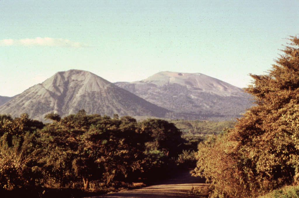 Two dramatically different volcano morphologies are visible in this photo of Las Pilas volcanic complex.  Conical 818-m-high Asososca stratovolcano (left foreground) has a pronounced erosional valley on its southern flank.  Broad Las Pilas volcano (right background) rises to 1088 m and has a more complex volcanic history.  These are the two most prominent of a roughly 30-km-long chain of N-S-trending vents. Photo by Jaime Incer, 1995.