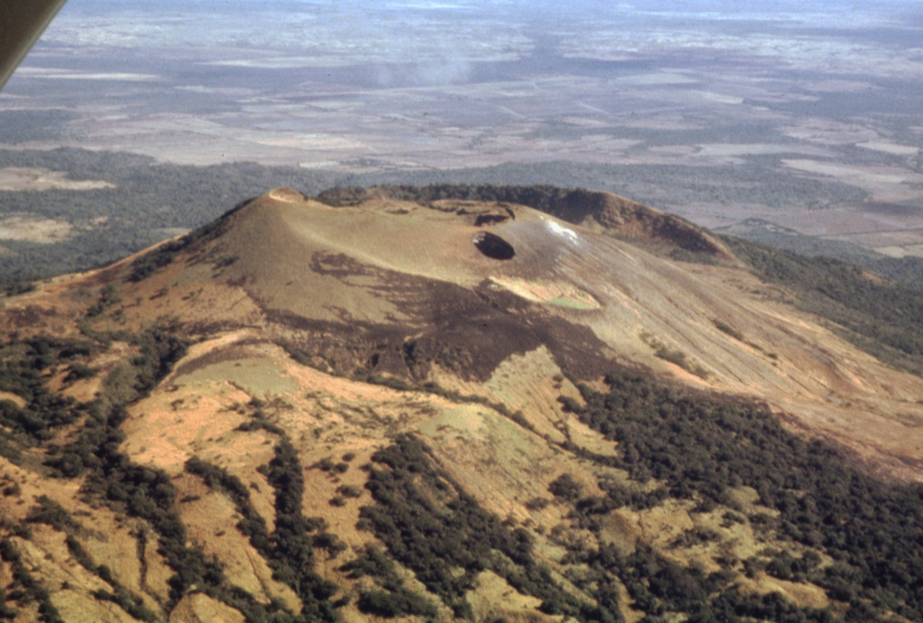 The flat light-colored area at the top of the photo beyond Las Pilas volcano in the foreground is the Malpaisillo caldera.  This large but topographically indistinct pyroclastic shield volcano lies in the Nicaraguan depression NE of Las Pilas volcano and NNW of Momotombo volcano.  Formation of the 10-km-wide Malpaisillo caldera produced extensively dissected dacitic airfall and ignimbrite deposits that extend across the graben east of the Marrabios Range and reach into Lake Managua to the SE.   Photo by Jaime Incer, 1995.