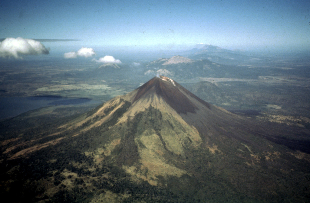 An aerial view to the NW looks down the spine of the Marrabios Range, which rises above the floor of the Nicaraguan depression.  In the foreground is Momotombo volcano, which rises to 1297 m above the shores of Lake Managua (left).  Monte Galán caldera lies beyond the right-hand flanks of Momotombo.  Stretching across much of the photo beyond Momotombo is the N-S-trending Las Pilas complex, and the conical peak in the far distance is San Cristóbal volcano. Photo by Jaime Incer, 1997.