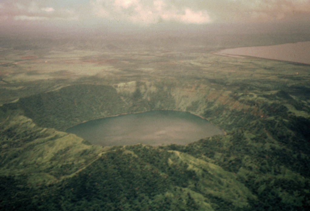Laguna de Apoyeque fills a 2.8-km-wide caldera constructed at the center of the Chiltepe Peninsula.  The caldera rim rises about 400 m above the lake, whose surface lies only about 40 m above sea level.  Two major pumice deposits erupted about 18,000-25,000 years ago originated from Apoyeque caldera.  The Lower Apoyeque pumice was erupted about 22,000-25,000 years ago, while the Upper Apoyeque pumice, which forms a distinctive layer in the Managua area, was erupted a few thousand years later.  Lake Managua lies at the upper right. Photo by Jaime Incer, 1996.