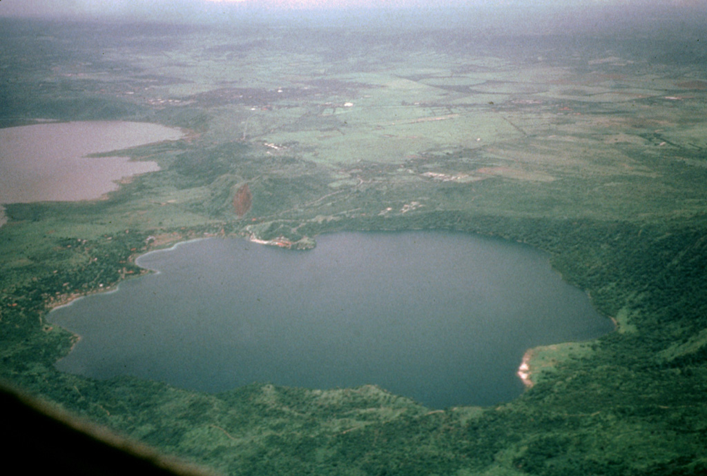 Laguna de Jiloa was the source of a major explosive eruption about 6500 years ago that deposited the widespread Jiloa Pumice, which blankets the Managua area.  Laguna de Jiloa (also spelled Xiloa) is seen here in an aerial view from the north with Lake Managua at the upper left.  The rim of the 2.5-km-wide caldera is lowest on the SE (left) and rises to 220 m on the NW side.  Cones of the Nejapa-Miraflores alignment can be seen extending to the south from the center of the far caldera rim. Photo by Jaime Incer, 1996.