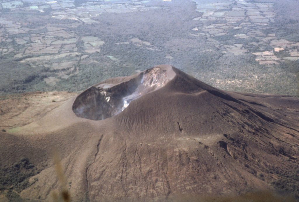 The 700-m-wide double summit crater of Telica volcano is seen here in an aerial view from the north with farmlands of the Nicaraguan depression in the background.  The 1061-m-high volcano is the highest and most recently active of the Telica volcanic complex.  The Telica volcano group consists of several interlocking cones and vents with a general NW alignment.  The bench at the lower right and the ridge at the left are remnants of older craters of the complex. Photo by Jaime Incer, 1991.