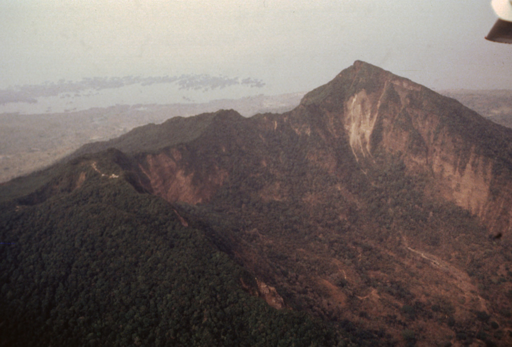 An aerial view of Mombacho from the SW shows the higher eastern summit of the twin-peaked volcano at the right.  In the foreground is the southernmost of two large collapse scarps that cut the edifice.  The other scarp, out of view on the NE flank beyond the ridge below the summit, was the source of a large debris avalanche that swept into Lake Nicaragua, forming the Aseses Peninsula and Las Isletas at the upper left. Photo by Franco Penalba (courtesy of Jaime Incer), 1994.
