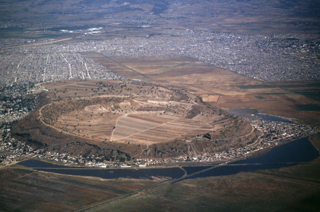 Xico is a low circular tuff ring within Mexico City that is part of the Chichinautzin volcanic field, seen here from the S. This volcano was formed by phreatomagmatic eruptions through the middle of Lake Chalco, the remains of which can be seen surrounding the tuff ring. Chalco and Lakes Texcoco and Xochimilco were formed when lava flows blocked river drainages to the S.  Photo by Hugo Delgado, 1994 (Universidad Nacional Autónoma de México).