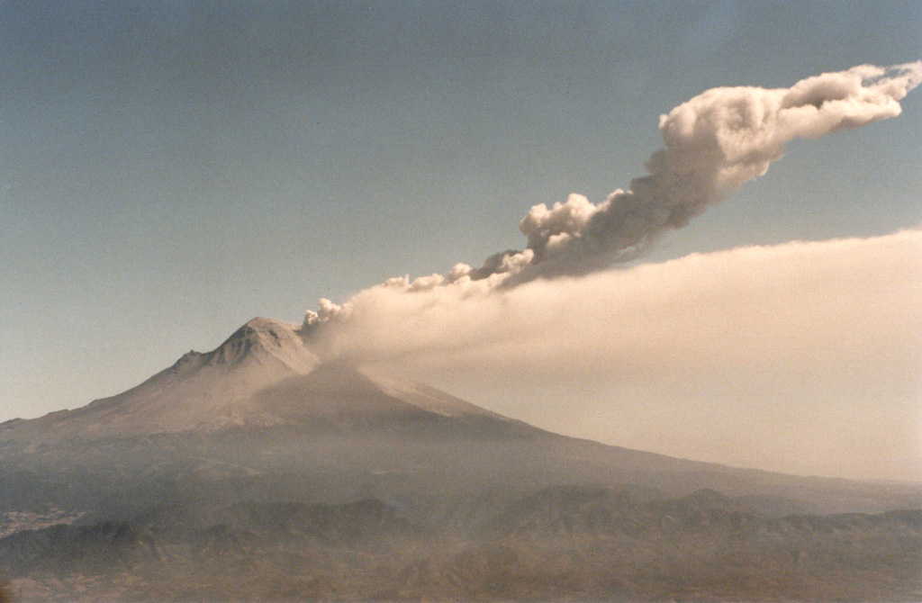 Two plumes are visible at Popocatépetl on 11 March 1996, six days after the renewal of explosive activity. A continuous diffuse plume disperses to the south at about 5,500 m elevation (roughly the height of the summit), while a second plume produced by a small explosion rises to about 8,000 m altitude. Beginning in 1996 multiple lava domes were extruded in the summit crater and periodically partially removed by explosions. Photo by Hugo Delgado-Granados, 1996 (Universidad Nacional Autónoma de México).
