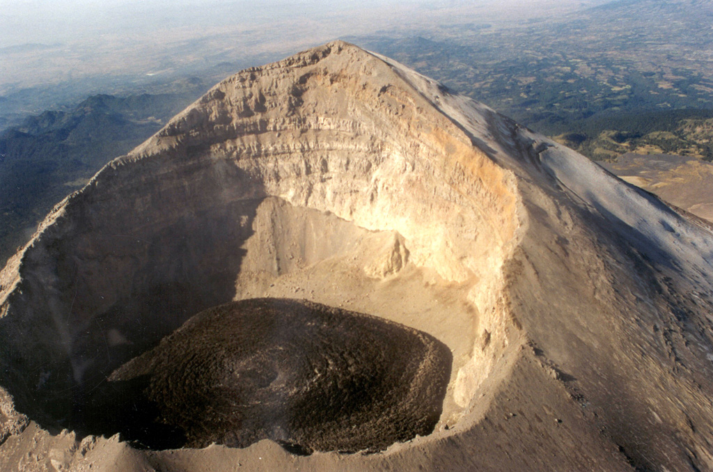 This photo shows the Popocatépetl summit crater with fresh lava visible on 9 December 1997 after rapid lava extrusion during 5-6 December had almost covered the entire crater floor. The high point on the WSW crater rim rises 450 m above the floor of the 700-m-wide crater. The stratigraphy of the upper cone is visible in the far crater wall.   Photo by Hugo Delgado-Granados, 1997 (Universidad Nacional Autónoma de México).