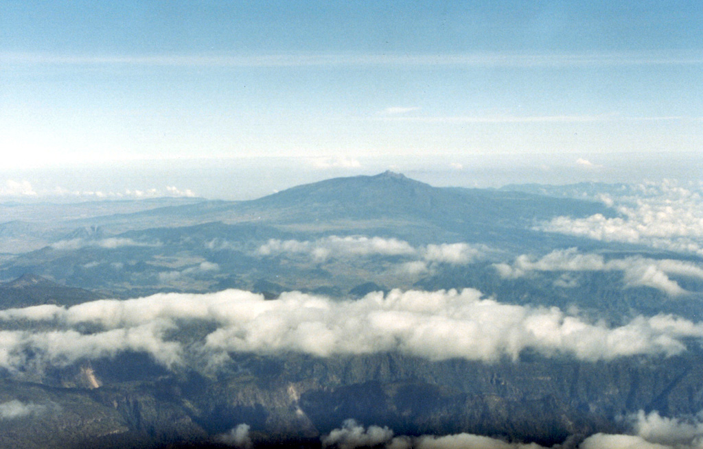 The broad Cofre de Perote massif in the distance is seen in an aerial view from the west. As with other volcanoes of the Orizaba-Cofre chain, it was constructed over the eastern margin of the Mexican altiplano, so that the volcano asymmetrically extends farther toward the lower-elevation coastal plain. It rises 1,700 m above the Serdán-Oriental basin on the west and 3,000 m above the city of Jalapa (Xalapa) to the east. Photo by Lucio Cardenas, 1996 (CENAPRED, courtesy of Hugo Delgado, Universidad Nacional Autónoma de México).