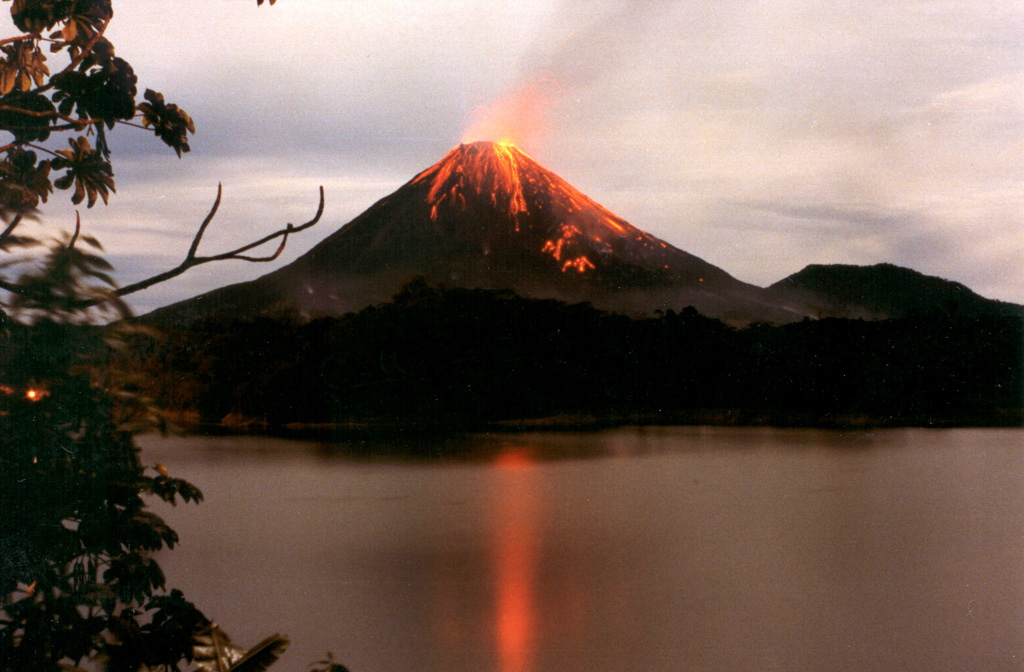 Strombolian eruptions from Arenal volcano are reflected in Lake Arenal in December 1992 during an eruption that began on 29 July 1968. The eruption produced major explosions and pyroclastic flows from three new vents on the west flank, destroying two towns and killing 78 people. The eruption continued through to 2010 and lava flows formed an extensive lava field on the west flank, accompanied by intermittent explosive activity. Photo by Olger Aragón, 1992.