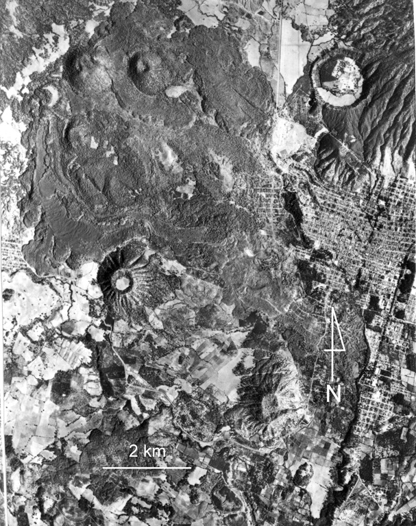 Cerro el Jabalí (upper left) and the adjacent Cerro el Sapien (immediately to the east) of the Michoacan-Guanajuato volcanic field produced the unvegetated lava flow extending across the top of the photo. Ashfall from Cerro el Jabalí scoria cone, located about 15 km SE of Parícutin, erupted about 3,830 years ago. The city of Uruapan is in the right side of the photo, south of the circular Costo (Cerro Cotji) maar. Aerial photo by Comisión de Estudios del Territorio Nacional (CETENAL).