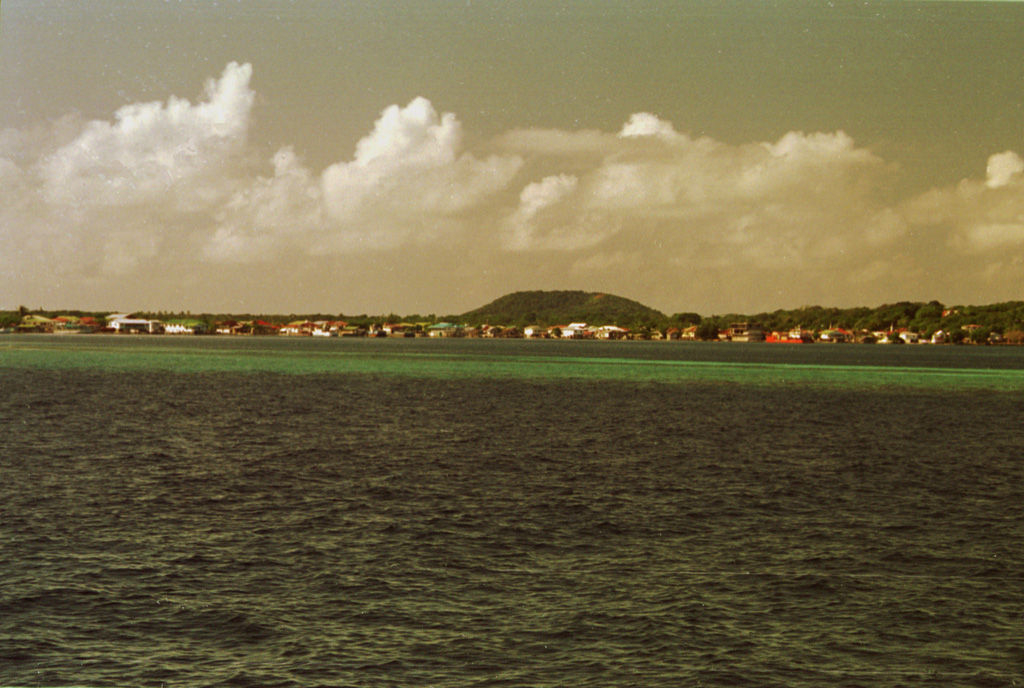 The low pyroclastic cone Stuert Hill (also spelled Stuart Hill) rises beyond Utila, the largest village on the island of the same name.  A ferry connects the village of Utila, formerly known as East Harbor, to the mainland of Honduras.  Most of the island consists of flat-lying uplifted coral reefs; volcanic rocks are found only at the eastern end of the island. Photo by Rick Wunderman, 1999 (Smithsonian Institution).