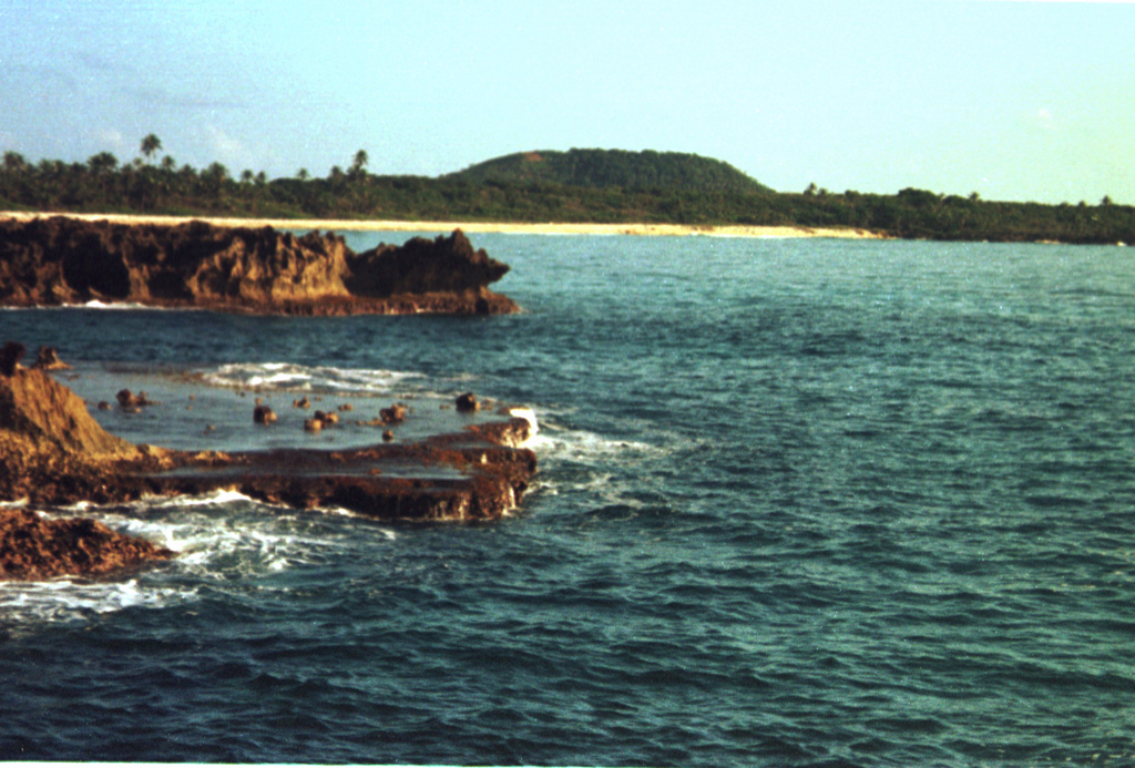 The low peak in the distance is Pumpkin Hill, a pyroclastic cone at the NE end of Utila Island.  The small 74-m-high cone was erupted onto a coral-capped erosional surface forming the cliffs in the foreground and marks the high point on the island.  Basaltic lavas and tuffs blanket terraces on the NE side of Utila.  The island lies in the Caribbean Sea off the northern coast of Honduras and is the easternmost and lowest of the Bay Islands at the southern edge of the submarine Bartlett Trough.   Photo by Rick Wunderman, 1999 (Smithsonian Institution).