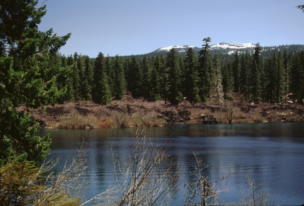 The snow-capped Sand Mountain scoria cones on the horizon were the source of the barren lava flow forming the far shore of Clear Lake. The lake formed when a series of lava flows erupted from the Sand Mountain volcanic field and traveled to the west, blocking the drainage of the ancestral McKenzie River. Standing stumps of the forest drowned by the rising lake waters have been radiocarbon dated to about 3,000 years ago and are still visible today. Photo by Lee Siebert, 1999 (Smithsonian Institution).