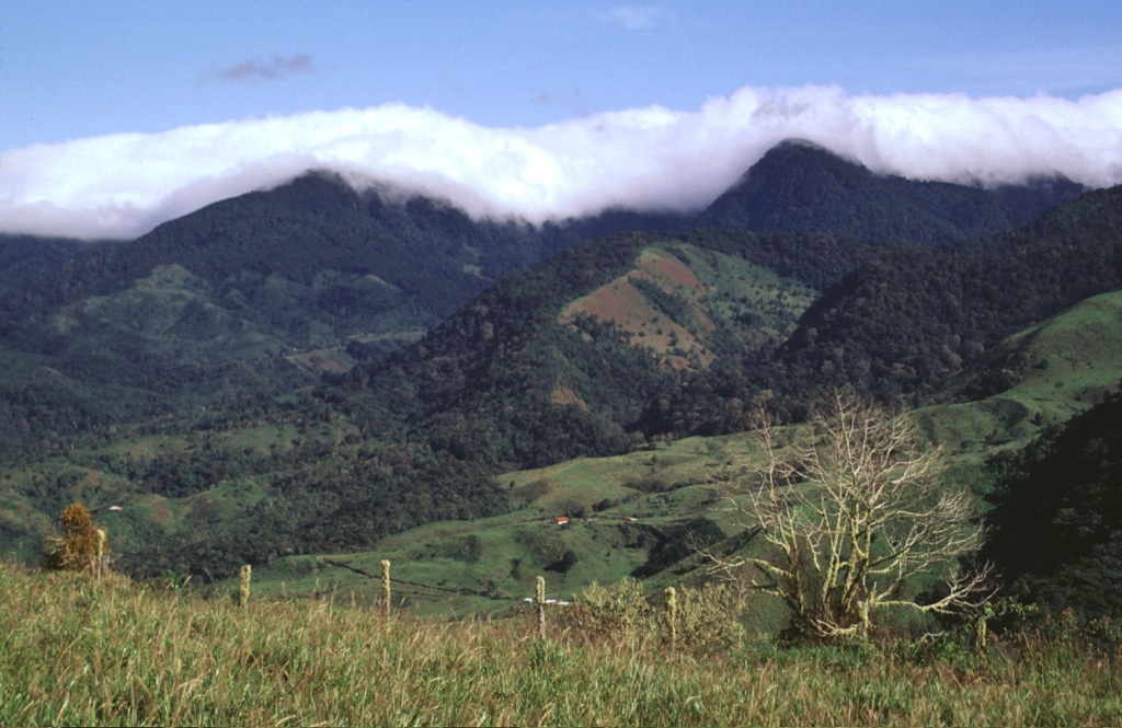 Clouds drape Cerro Totuma (left) and Cerro Pelón (right), post-caldera lava domes of Volcán Tsingal (Cerro Colorado).  The volcano lies in the Talamanca Range of westernmost Panama, next to the Costa Rica border NW of Volcán Barú.  The photo is taken from Cerro Pando, a lava dome that lies on the southern side of the volcano, opposite a 7-km-wide caldera that is breached widely to the SW.  Potassium-Argon ages for the Volcán Colorado complex range from 1.66 million years to 0.52 million years. Photo by Lee Siebert, 1998 (Smithsonian Institution).