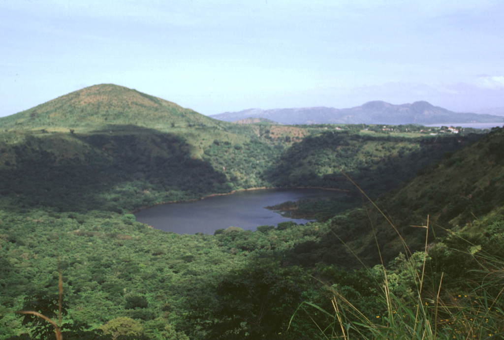 Cerro Motastepe cinder cone (upper left) is the youngest and most prominent feature of the Nejapa-Miraflores volcanic alignment.  The cone, seen here from the SE with Laguna de Nejapa in the center of the photo, is elongated in an E-W direction and rises 160 m above its base to 360 m elevation.  Cerro Motastepe formed less than 2500 years ago.  The surface of saline Laguna de Nejapa collapse pit (center) lies at about the same level as Lake Managua, barely visible in the distance at the upper right.  Photo by Lee Siebert, 1998 (Smithsonian Institution).