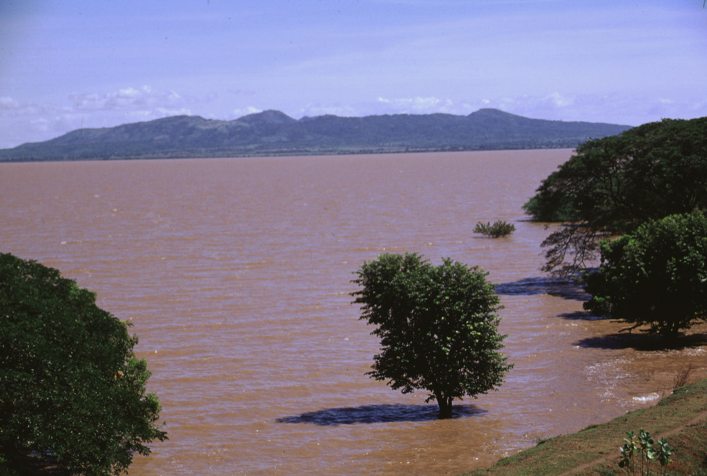 The broad Chiltepe Peninsula rises to the SE across the flood-stained waters of Lake Managua.  Apoyeque caldera lies beyond its horizontal rim on the right-center horizon.  The 11-km-wide peninsula extends into Lake Managua and marks the northern limit of a segment of the central Nicaraguan volcanic chain that is offset to the east. Photo by Lee Siebert, 1998 (Smithsonian Institution).