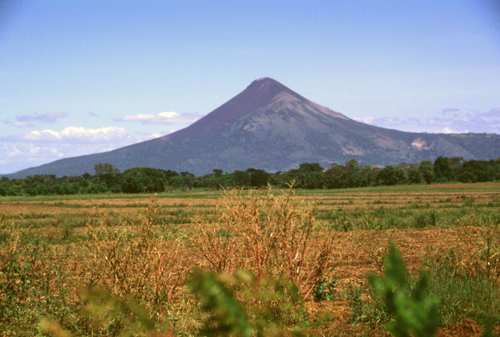 Momotombo volcano towers above the floor of the Nicaraguan depression.  Following its birth about 4500 years ago, a catastrophic eruption of Old Momotombo volcano about 2700-2800 years ago produced large amounts of tephra and pyroclastic flows.  As a result of this eruption a 1.5 x 1.1 km wide crater was formed at the summit.  Subsequent eruptions beginning about 800-900 years ago created the Young Momotombo volcano, which filled much of this crater and forms the present summit. Photo by Lee Siebert, 1998 (Smithsonian Institution).