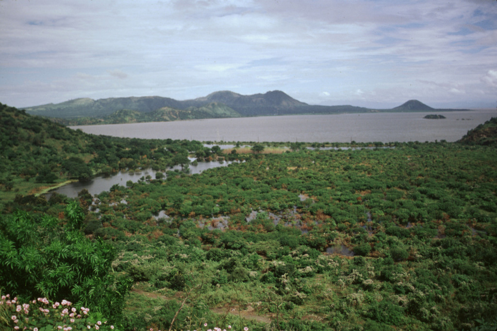 The Chiltepe Peninsula is seen across Lake Managua from the south on the outskirts of the city of Managua.  The broad peninsula extends into the lake about 6 km north of the city and lies at the northern end of a chain of pyroclastic cones and craters that extends into the city.  The small conical peak on the far right horizon is Volcán Chiltepe. Photo by Lee Siebert, 1998 (Smithsonian Institution).
