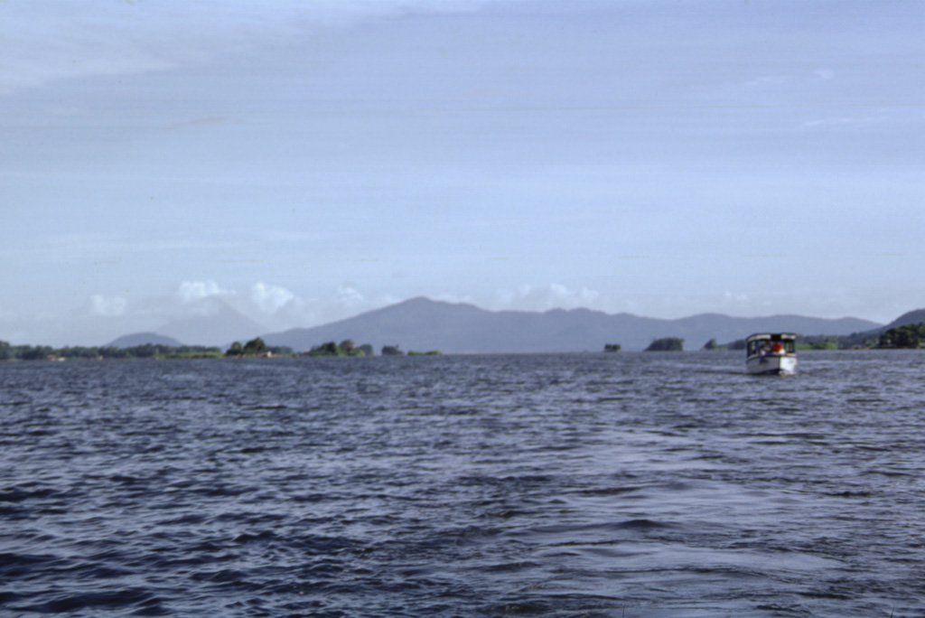 A small boat plies the waters of Ensenada de Aseses, with Zapatera Island forming the horizon to the SE.  In the middle distance are the small island hummocks of Las Isletas, formed by a debris avalanche from Mombacho volcano, out of view to the right.  The conical peak on the distant left horizon is Concepción volcano; the low, rounded peak to its left is Cerro las Banderas, a pyroclastic cone on the NE tip of Zapatera Island. Photo by Paul Kimberly, 1998 (Smithsonian Institution).