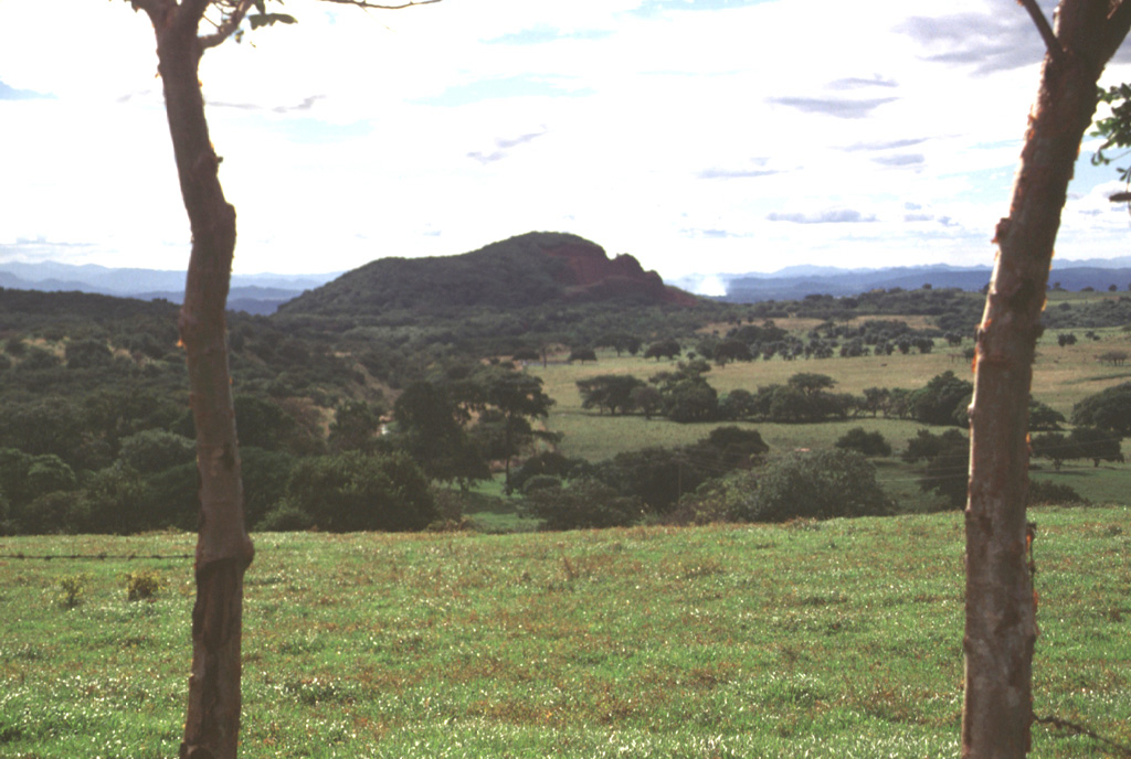 The small pyroclastic cone Cerro Chopo (also known by the religious names of Anunciación, Coronación, or Asunción) is seen here from the ENE along the road between Canas and Tilarán south of the Guanacaste Range.  The 250-m-high basaltic pyroclastic cone was constructed over the flat-lying surface in the foreground, which is underlain by Pleistocene regional ignimbrites, lahars, and andesitic lava flows.  The age of the cone has been roughly estimated to be between 40,000 and 10,000 years old.  Photo by Lee Siebert, 1998 (Smithsonian Institution).