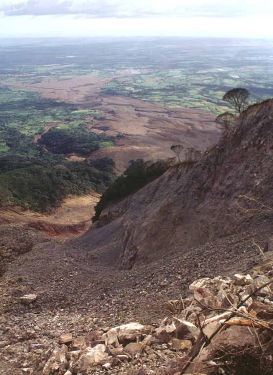 The course of the devastating debris avalanche and mudflow of October 30, 1998, is seen here from the top of the headwall scarp.  Collapse of a relatively small area in the foreground (the western collapse scarp is the bare ridge at the right center) near the summit of Casita volcano produced an avalanche that transformed into a devastating mudflow and inundated lowland areas in the distance.  The lahar overran two towns, which were located at the area in the sunlight at the upper left.  The Pacific Ocean forms the horizon. Photo by Lee Siebert, 1998 (Smithsonian Institution).