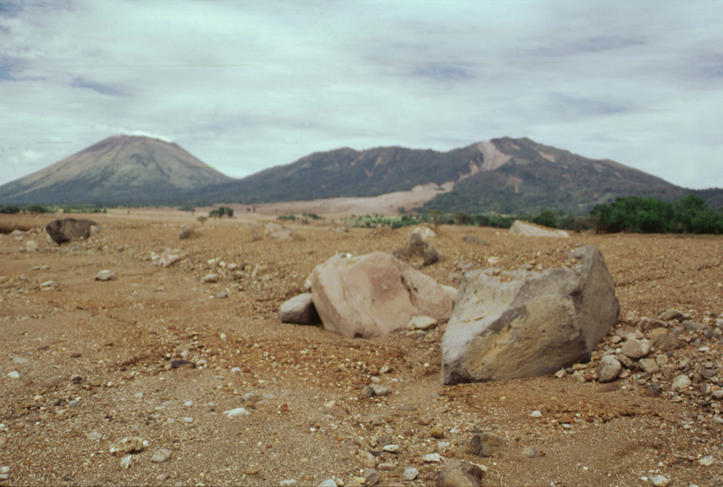 Rapidly moving fine-grained sediment and coarse boulders of a devastating lahar on 30 October 1998 obliterated evidence of the towns of El Porvenir and Rolando Rodriguez, which were located in the foreground area of this photo.  The trace of the mudflow forms the light-colored scar extending from its source near the summit of Casita volcano (upper right).  The devastating mudflow, which killed about 1600 people, was about 3 m deep at peak flow and 1.5 km wide at the location of the two towns.  San Cristóbal volcano is at the upper left. Photo by Paul Kimberly, 1998 (Smithsonian Institution).