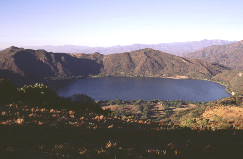 The scenic lake-filled Santa María del Oro maar, erupted through older Miocene rhyolitic tuffs, is one of the many dramatic volcanic features of the Tepic-Chapala graben.  The southern rim of the maar (foreground) is reached by a road from the town of Santa María del Oro.  The peaks of Cerro Los Lobos form the northern rim on the far side of the maar and rise about 400 m above the Laguna Santa María crater lake.  Pyroclastic-surge deposits occur in valleys to the north and in some cases along the walls of the crater.  Photo by Lee Siebert, 1997 (Smithsonian Institution).