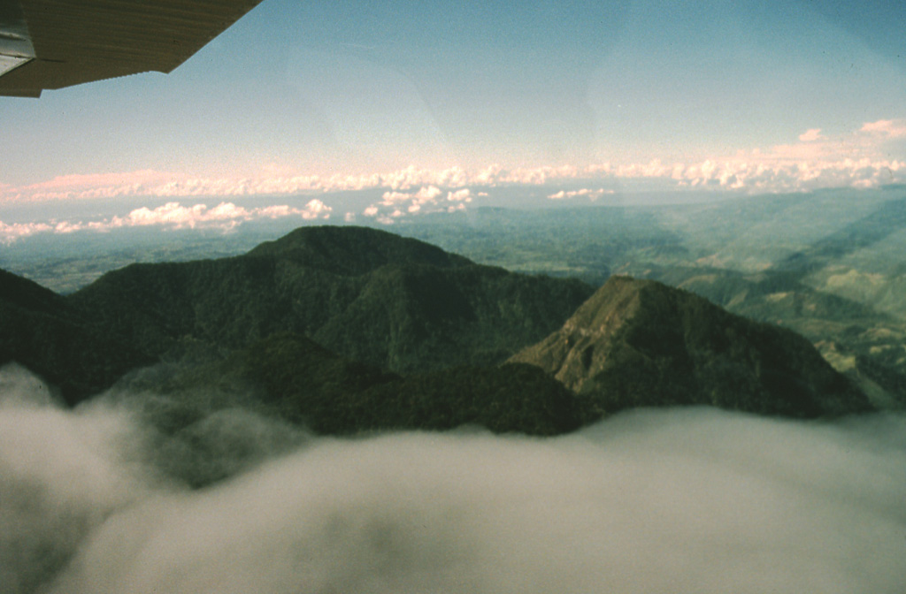 Two post-caldera lava domes of Volcán Colorado are seen here from the NE.  The forested dacitic 2679-m-high Cerro Pelón lava dome is at the left center and andesitic 2625-m-high Cerro Totuma is the lava dome at the right.  Roughly 1400-year-old tephra deposits on top of Cerro Totuma originated from Volcán Barú.  The northern caldera rim can be seen just above the cloud layer, in front and to the left of Cerro Totuma.  The caldera is breached widely to the SW, in the direction of Costa Rica in the background. Photo by Kathleen Johnson, 1998 (New Orleans University).