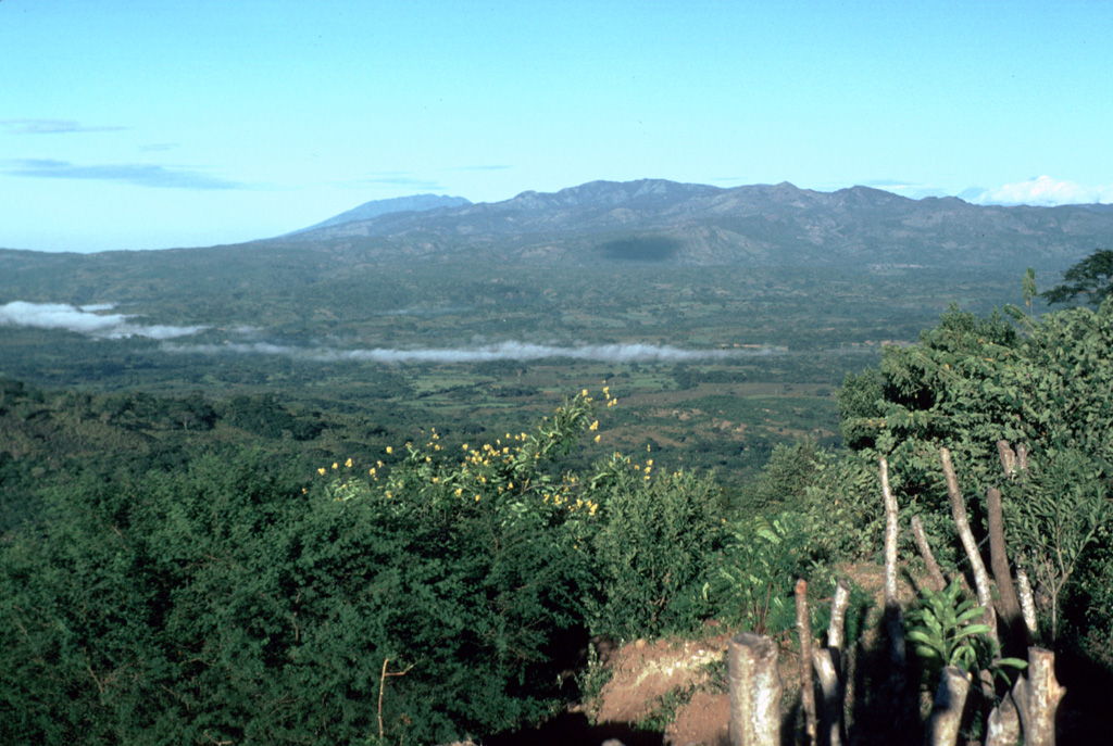 Morning fog drapes the valley of the Río Margarita, with Ixhuatán volcano in the background.  The broad summit of Tecuamburro volcano is visible to the west behind Ixhuatán on the horizon left of center.  Los Ochiotes complex in the center of Ixhuatán volcano is the youngest part of the volcano and consists of a group of dacitic lava domes that fills a horseshoe-shaped depression open to the SE.  Photo by Lee Siebert, 1988 (Smithsonian Institution).