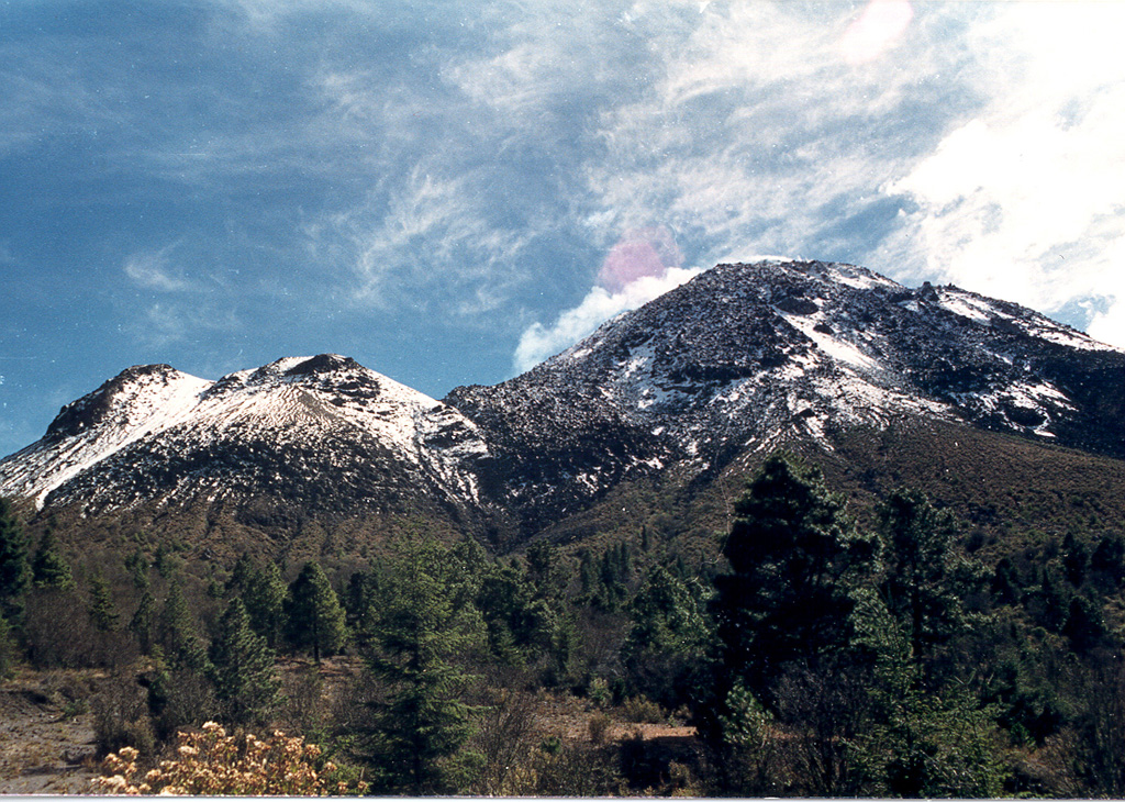 The two rounded peaks to the left, 700 m below and 1 km NE of the summit of Colima, are the El Volcancito lava-dome complex, with dome growth commencing on 12 June 1869 after large explosive eruptions. Deformation had been visible with the naked eye since 19 March. During the eruption 0.21 km3 of lava filled the NE part of the caldera, and lava flows from Volcancito flowed to the ESE and ENE over the caldera rim. Photo by Guillermo Castellano, 1990 (courtesy of Jim Luhr, Smithsonian Institution).