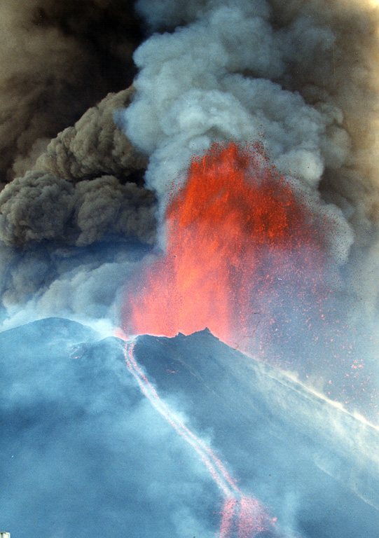 A lava fountain and ash plumes erupt above MacKenney crater at Pacaya during a major eruptive episode on 16 January 2000. A lava flow is also descending the northern flank of the cone. After a quiescent period of nine months, eruptive activity had been more or less continuous at Pacaya since January 1990. Activity has consisted of frequent moderate eruptions that constructed the summit cone, punctuated by occasional larger explosions such as this one that enlarge the crater and reduce the height of the cone. Photo by Gene West, 2000.