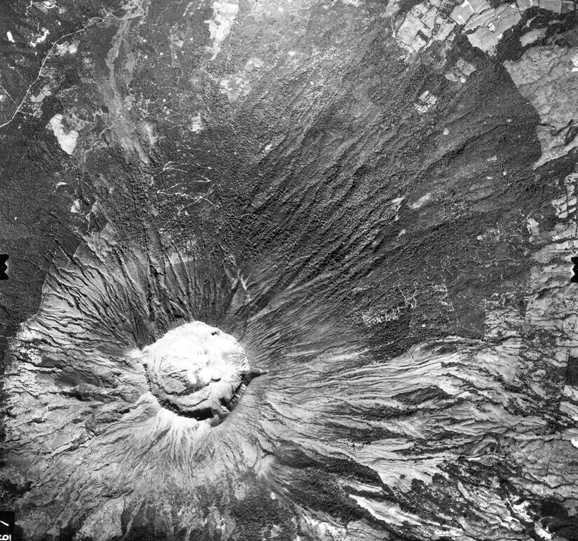 The symmetrical cone of San Miguel is truncated by a deep, 900-m-wide crater.  Benches on the crater floor reflect a complex history of modification of the crater during historical time.  The upper unvegetated part of San Miguel volcano is dissected by erosional gullies.  Many lava flows have originated from flank vents, including those at the lower right and the dark-colored, sparsely vegetated flow crossed by the highway at the upper left.  The latter was erupted in 1844. Aerial photo by Instituto Geográfico Nacional El Salvador.