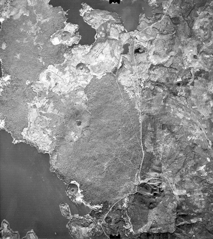 Young lava flows from Volcán de San Diego (left center) extend into Lake Güija (lower left).  The prominent cinder cone on the lake shore directly south of Volcán de San Diego is Cerro el Tule.  Young basaltic lava flows from other vents of the San Diego volcanic field in western El Salvador, such as Cerro la Vega de la Cana and Loma Iguana (upper left), extend into both Lake Güija and Laguna de Metapán at the top of the photo.  The cinder cone north of Volcán de San Diego (surrounded by older lava flows) is Cerro Masatepeque. Aerial photo by Instituto Geográfico Nacional El Salvador, 1977.